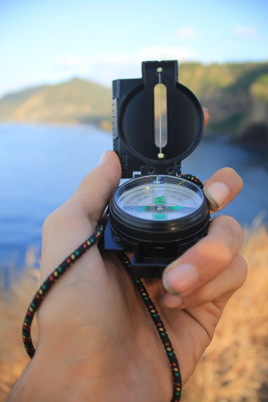 person, holding, black, compass, front, ocean water, daytime, shallow, focus photography, way