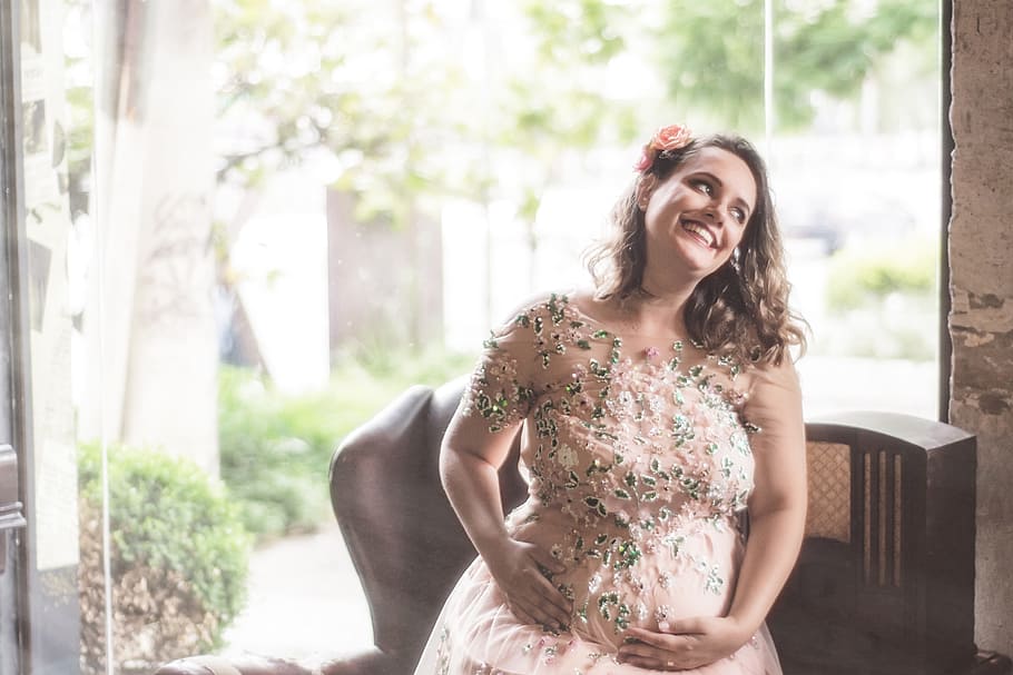 pregnant, woman, beige, floral, dress, sitting, brown, wooden, sofa, smiling