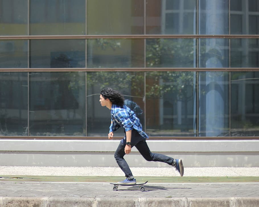 man, riding, skateboard, front, clear, glass building, wearing, blue, plaid, long