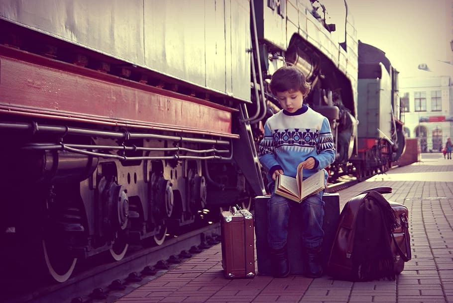 boy opening book page, sitting, luggage, train, outdoors, people, baby, portrait, kids, railway