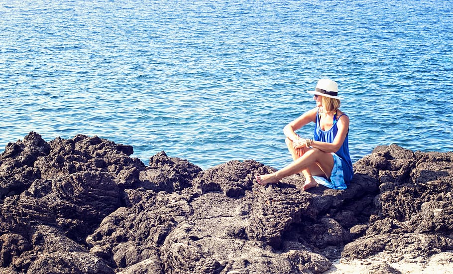 woman, blue, scoop-neck sleeveless dress, sitting, black, rock, ocean, daytime, rocks, dress