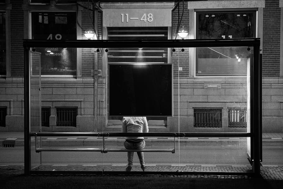 persona, sentado, banco, al lado, edificio de cristal, noche, parada de autobús, esperando, transporte público, urbano