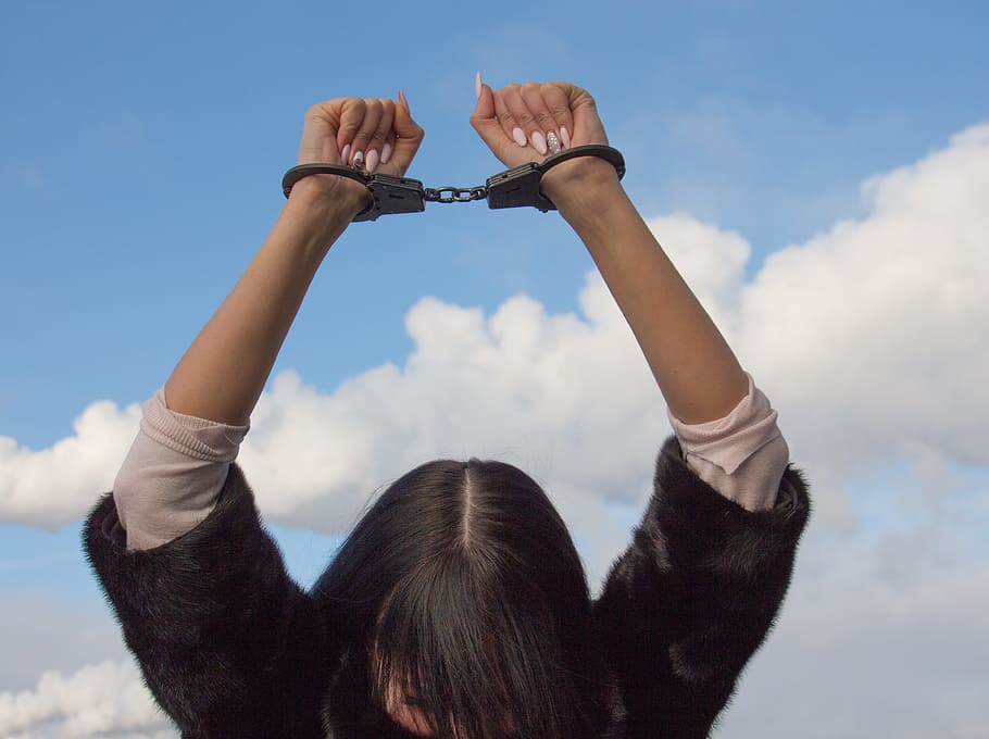 woman, wearing, black, white, shirt, raising, hands, gray, handcuffs, daytime