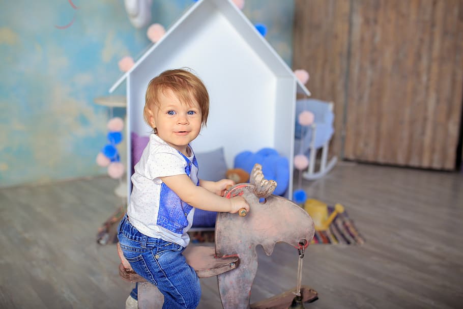 toddler, wearing, white, blue, riding, brown, animal toy, baby, happy, joy