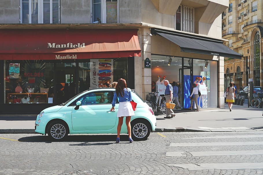 Mujer, de pie, sosteniendo, azul, Fiat 500, izquierda, estacionamiento en la puerta, calle, arquitectura, edificio