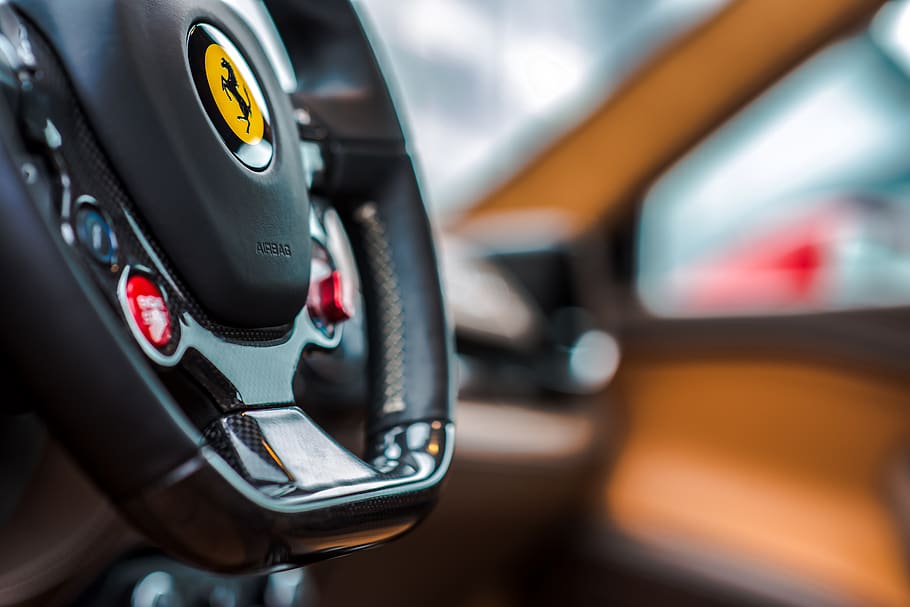 ferrari steering wheel, the ferrari logo in yellow, engine start button, background, car flyer, luxury car, transportation, mode of transportation, focus on foreground, close-up