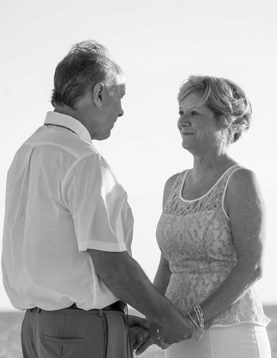 greyscale photography, man, woman, facing, holding, hands, wide, field, beach wedding, happy couple