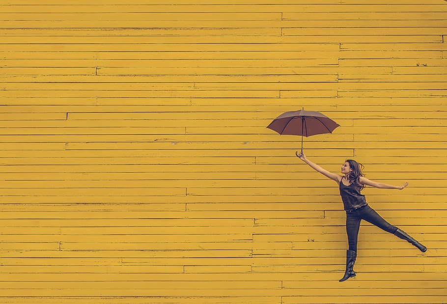 mujer, tenencia, paraguas, amarillo, fondo, flotante, saltando, fondo amarillo, artístico, urbano