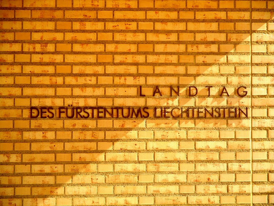 architecture, brick light, sunlight, golden, caption, landtag of principality of liechtenstein, vaduz, text, western script, wall