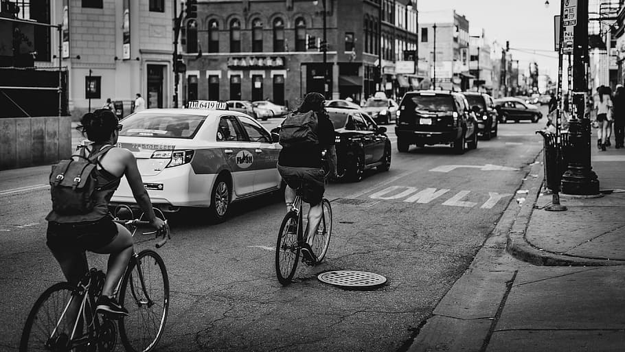 greyscale photo, people, bike, riding, along, cars, road, buildings, greyscale, bike riding
