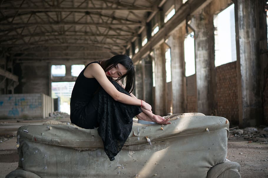 woman, sitting, sofa, wearing, black, sleeveless maxi dress, holding, arms, inside, abandoned