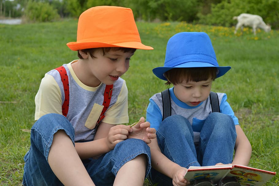 two, kids, wearing, orange, blue, fedora hats, sitting, grass, meadow, field