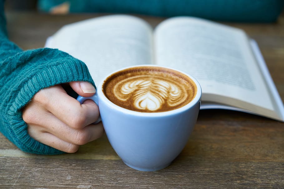person, holding, blue, ceramic, cup, coffee, inside, book, behind, beverage