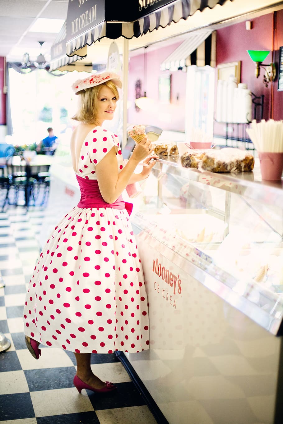 woman, wearing, white, pink, polka-dot cap-sleeved dress front, clear, glass display counter, vintage ice cream parlor, pretty young woman, vintage
