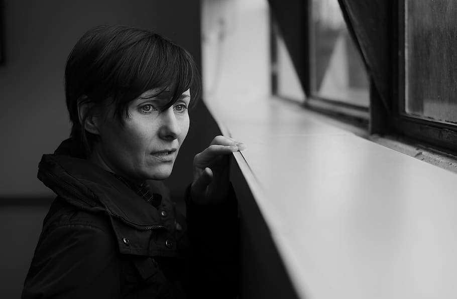 greyscale photo, woman, wearing, coat, looking, window, sad, grief, black and white mono, adult