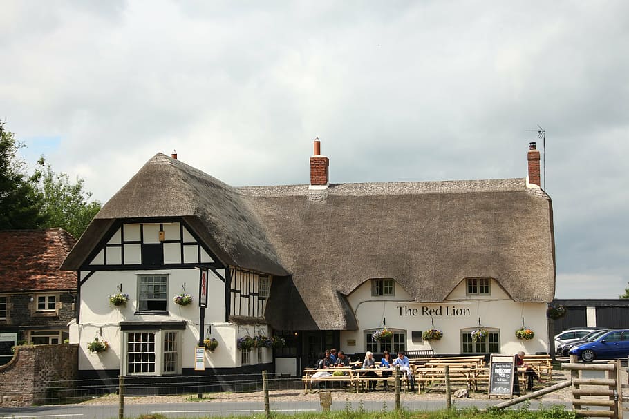 person, standing, front, red, lion building, daytime, avebury, thatched cottage, inn, pub