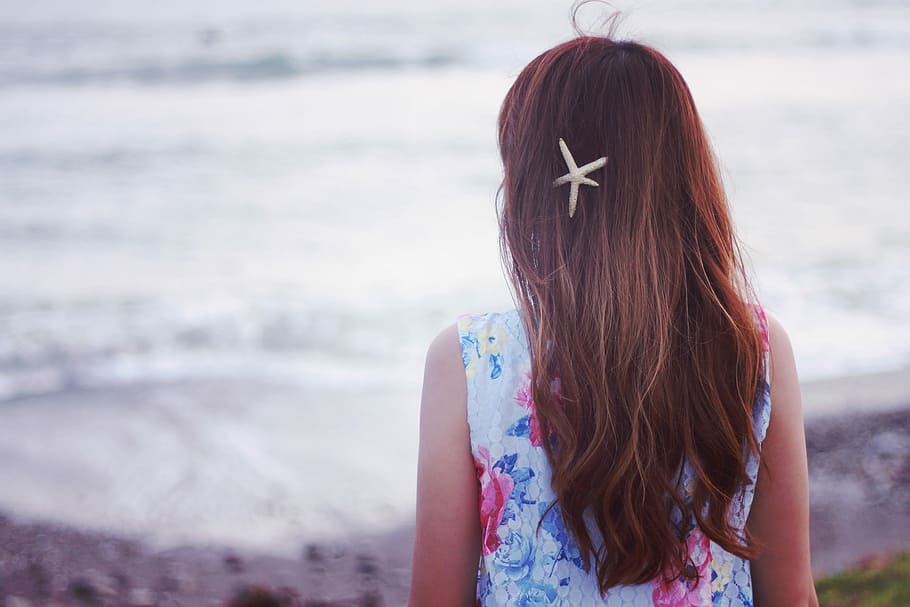 girl, wearing, white, floral-pattern sleeveless shirt, starfish hairclip, facing, backwards, beach, daytime, floral