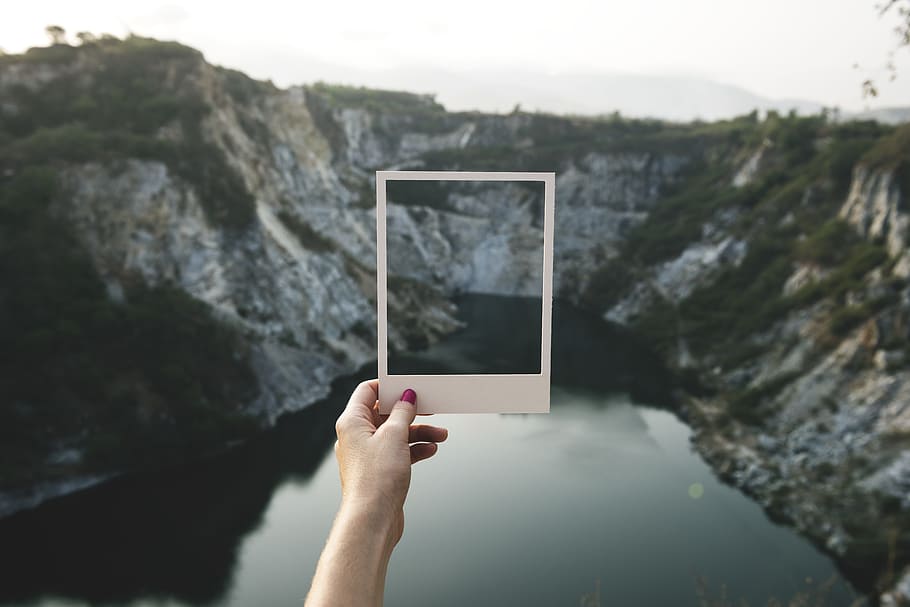 person, holding, white, frame mirror, facing, mountain, daytime, calm, rocky, stone