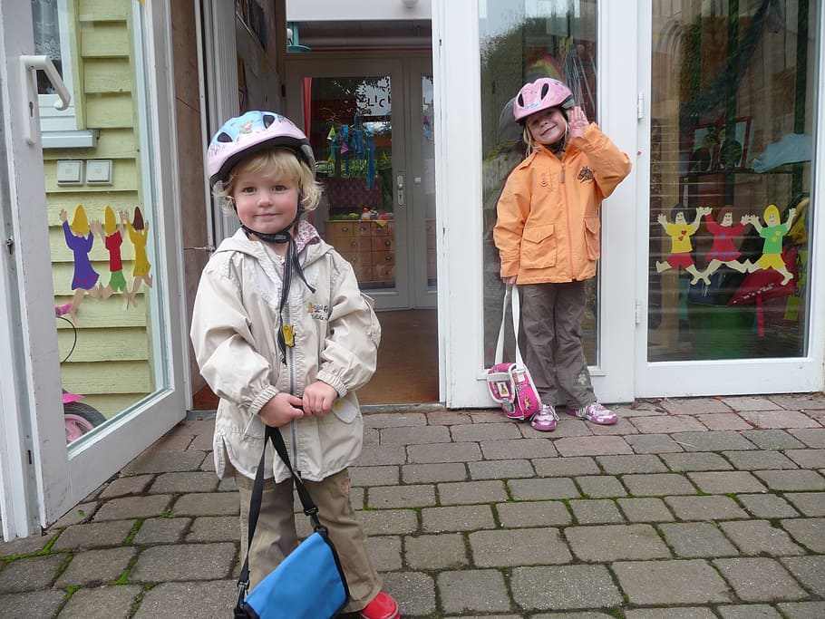 dois, crianças, vestindo, jaquetas, capacetes de bicicleta, jardim de infância, saco de berçário, feliz, porta, criança