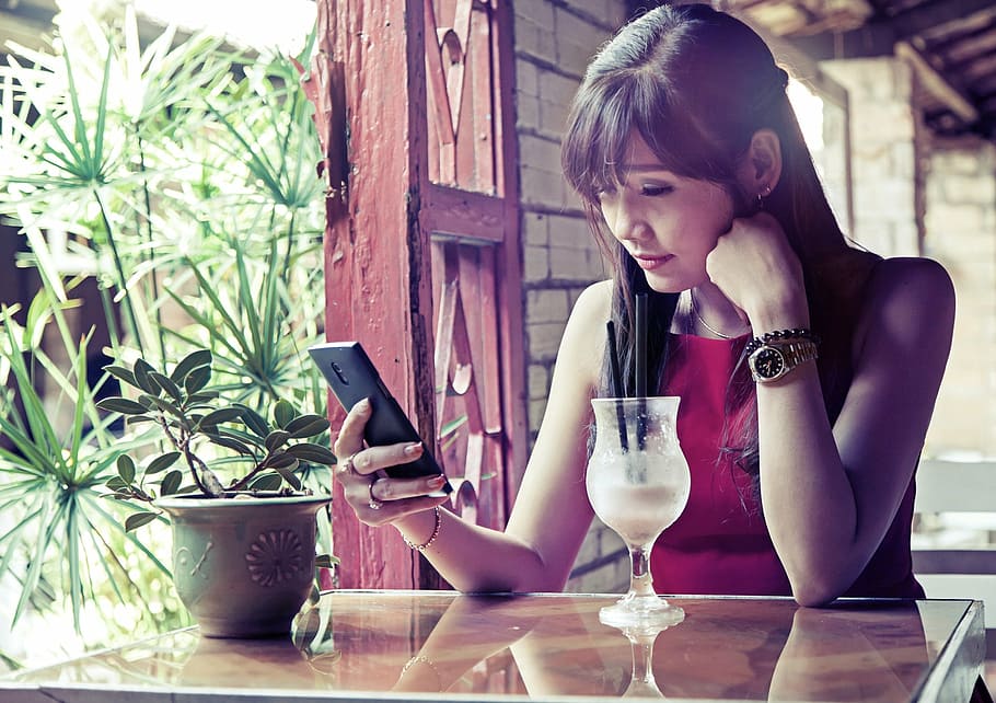 woman, wearing, red, sleeveless, top, using, smartphone, sitting, table, sad status
