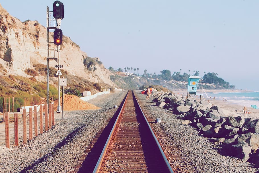 trem ferroviário, beira mar, homem, em pé, próximo, mar, dia, trilhos de trem, seixos, rochas