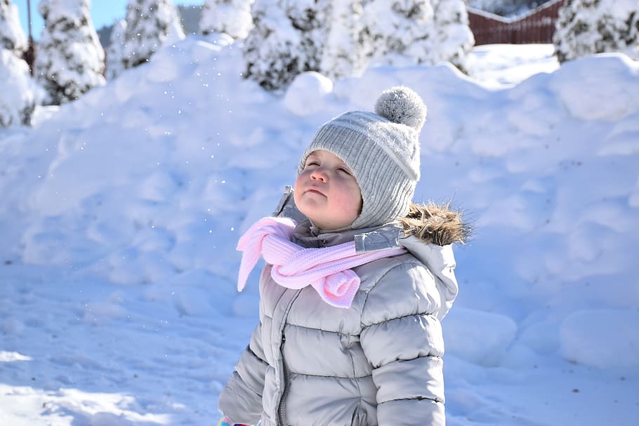 girl, wearing, gray, puffer hooded jacket, knitted, bobble hat, snow, baby, white, happy