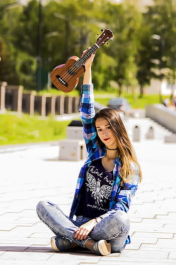 Beautiful young woman playing a black guitar while keeping her leg on a  stool Photo