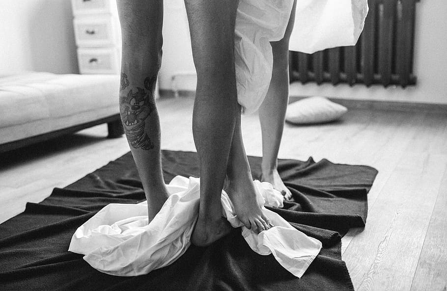 grayscale photo, couple, standing, rug, feet, legs, people, girl guy, tattoo, bed sheet