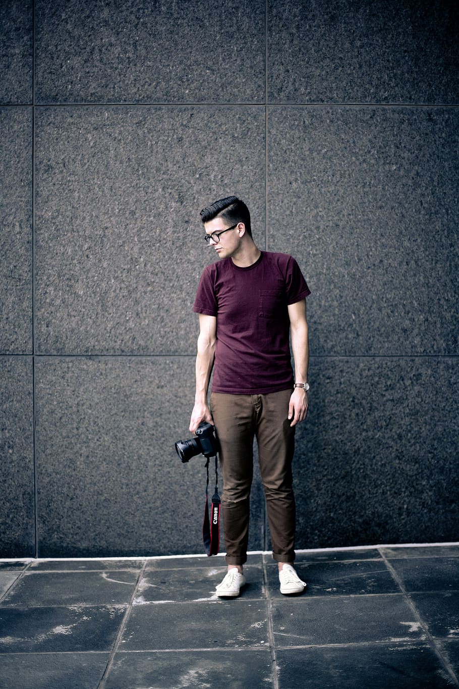 man, maroon, crew-neck t-shirt, holding, canon dslr camera, standing, wall, adult, business, camera