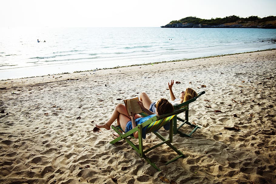 two, women, sitting, sling chairs, front, sea, beach, book, calm, casual