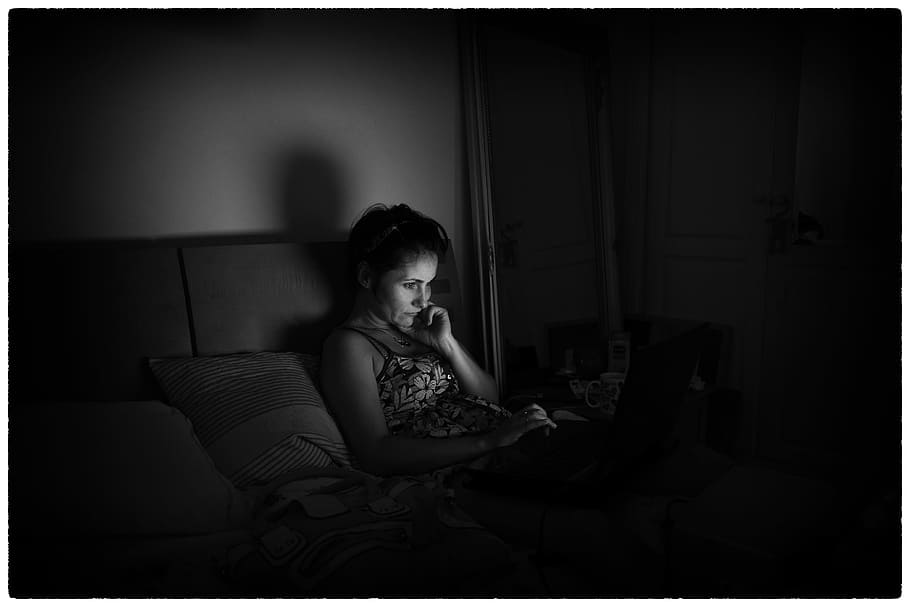 grayscale photograph, woman, lying, bed, using, laptop, computer, screen, light, darkness