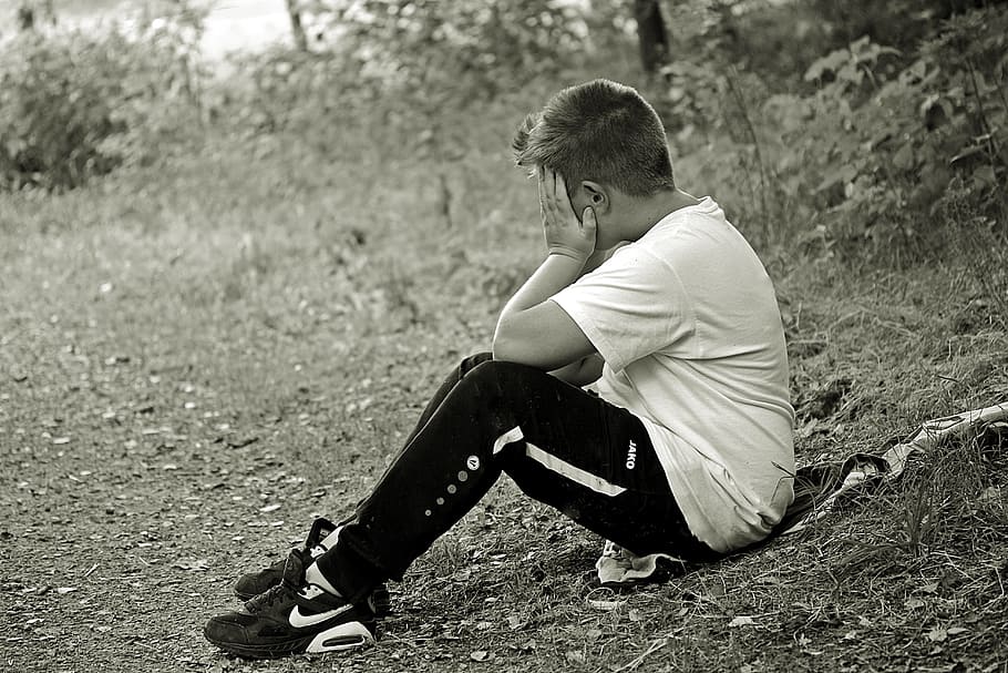 grayscale photo, man, holding, face, sitting, grass field, boy, child, sad, alone