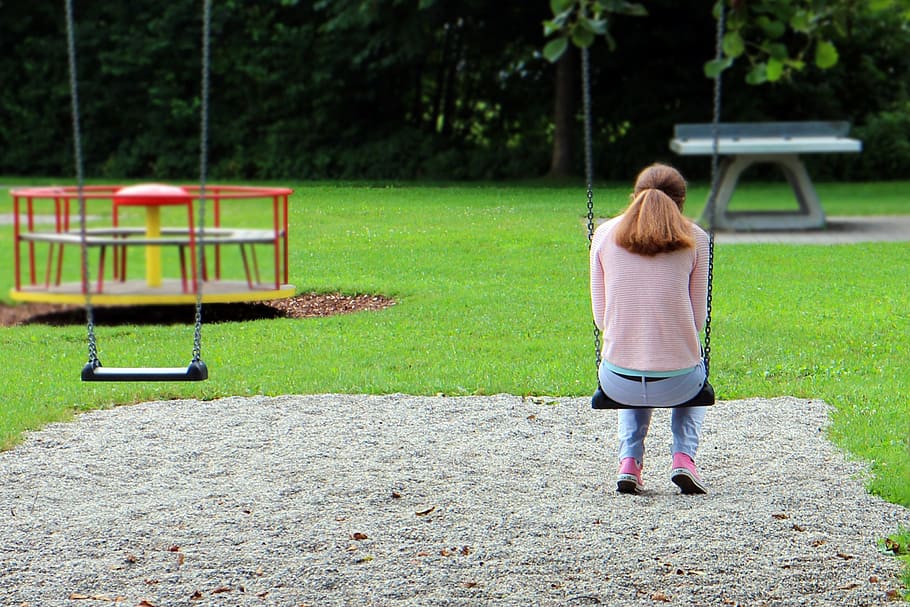 woman, pink, sweater, blue, denim pants, sitting, swing, facing, back, playground