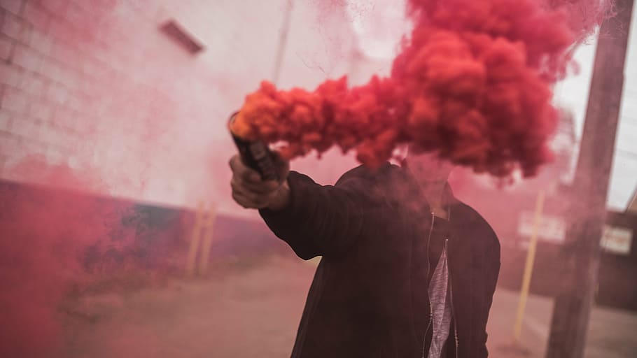 person, standing, wall, holding, red, smoke, daytime, man, guy, color
