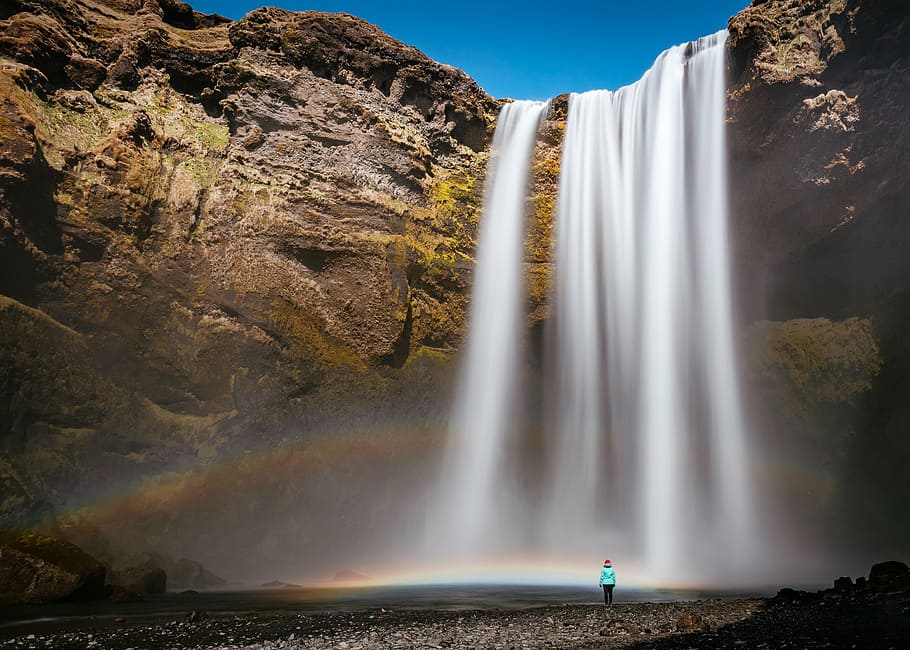 person, standing, waterfall, hill, rocks, water, blue, sky, nature, rainbow