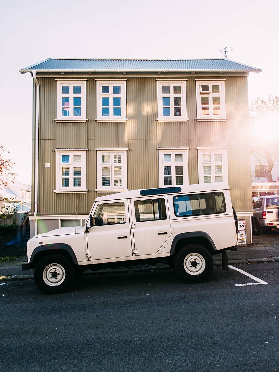 white, land rover defender suv, parked, front, brown, 3-story, 3- story building, gray, clouds, white Land
