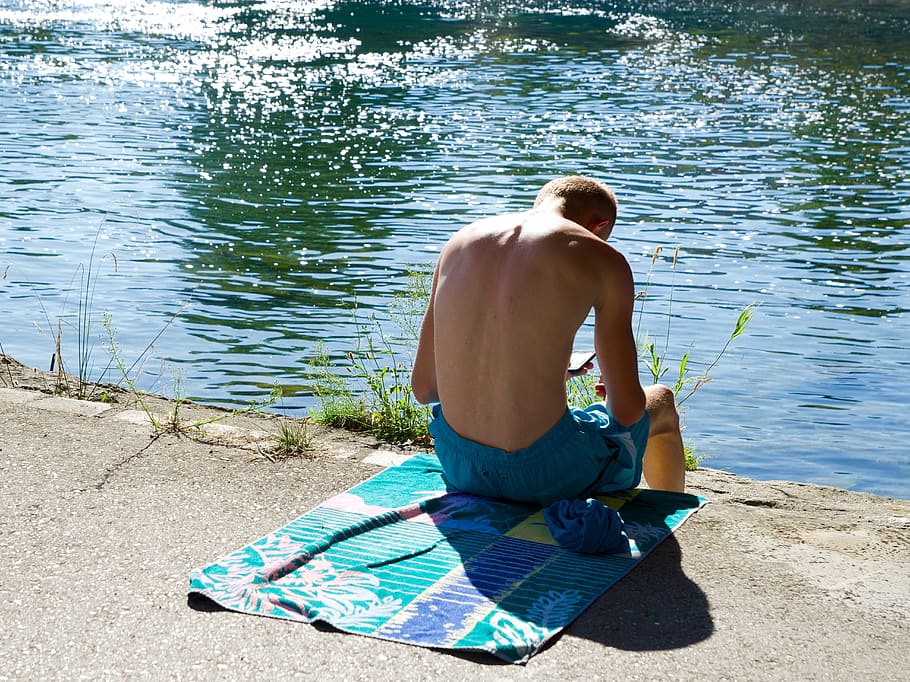 swimming trunks, bath towel, on the water, bathing, iphone, water, sitting, leisure activity, rear view, one person
