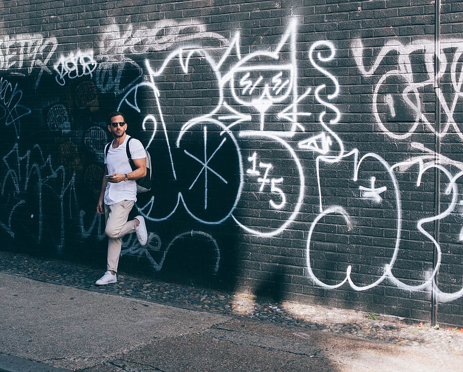 homem, vestindo, branco, camiseta, inclinando-se, parede, grafite, arte, vandalismo, oculos de sol