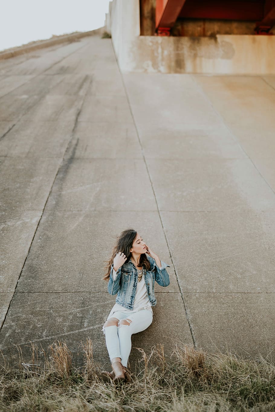 woman, blue, washed, denim jacket, white, shirt, distressed, jeans, leaning, concrete