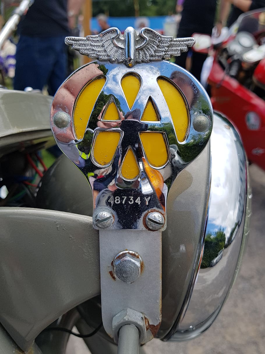 aa, badge, motorcycle, logo, sign, emblem, insignia, focus on foreground, close-up, incidental people