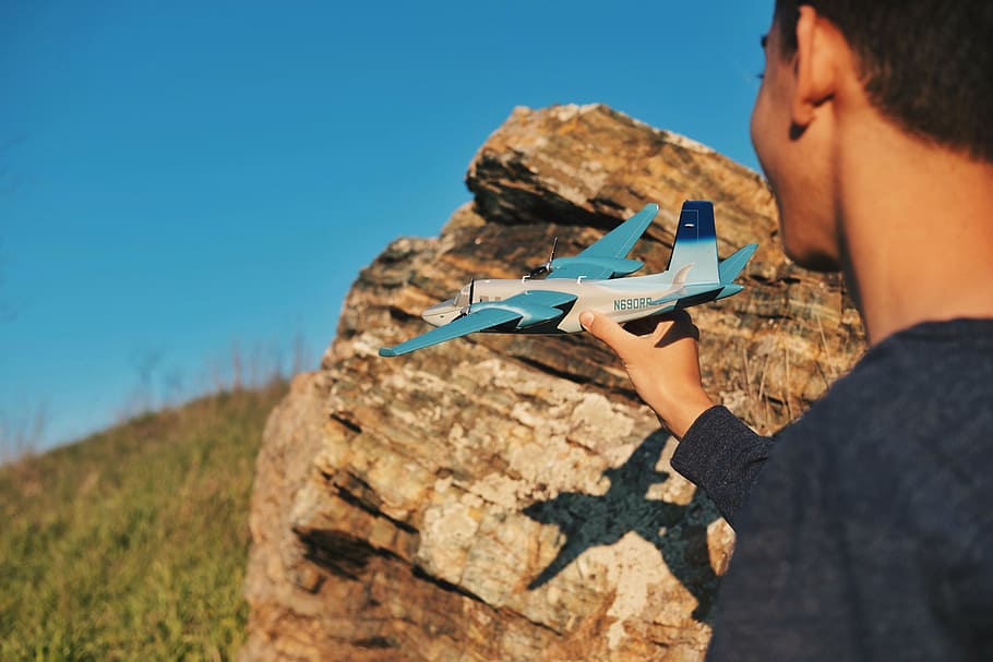 boy, holding, toy plane, airplane, airline, toy, blue, sky,green, grass, rocks
