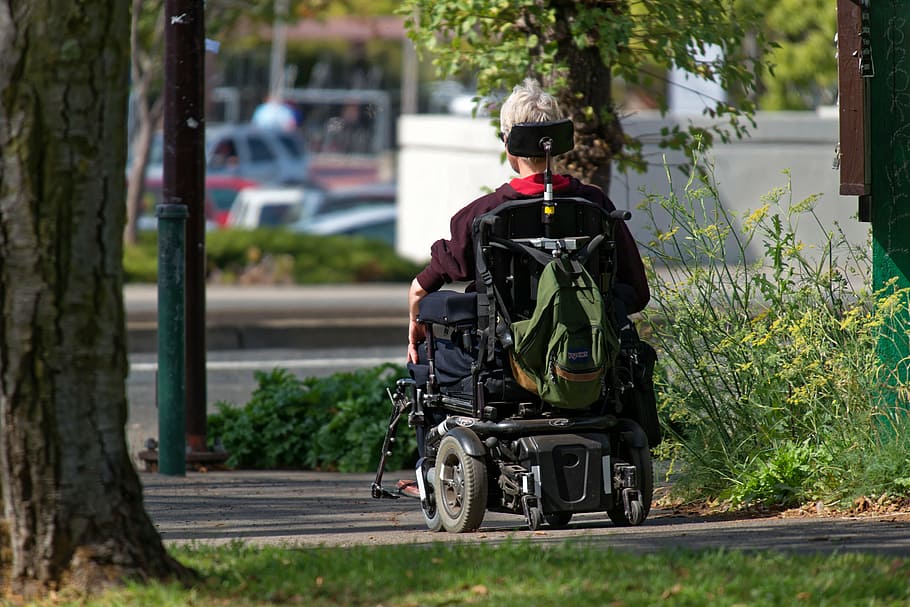 person, wheelchair, sidewalk, motorized wheelchair, elderly, man, motorized, backpack, sunny day, pavement