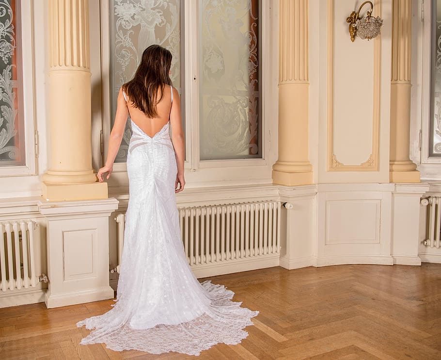 woman, white, backless wedding gown, standing, beige, concrete, pillar, inside, room, floral-etched glass window panels