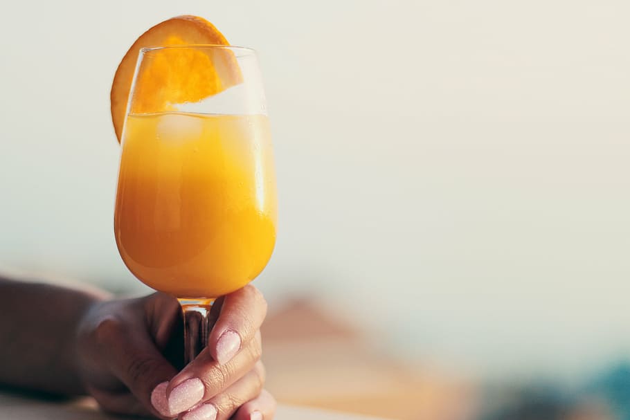 person, holding, orange, juice, goblet glass, clear, wine, glass, daytime, orange juice