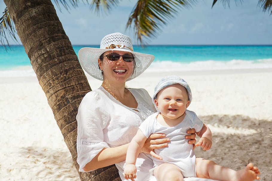 mulher, sorridente, vestindo, chapéu de sol, segurando, bebê, sentado, colo, azul, verão