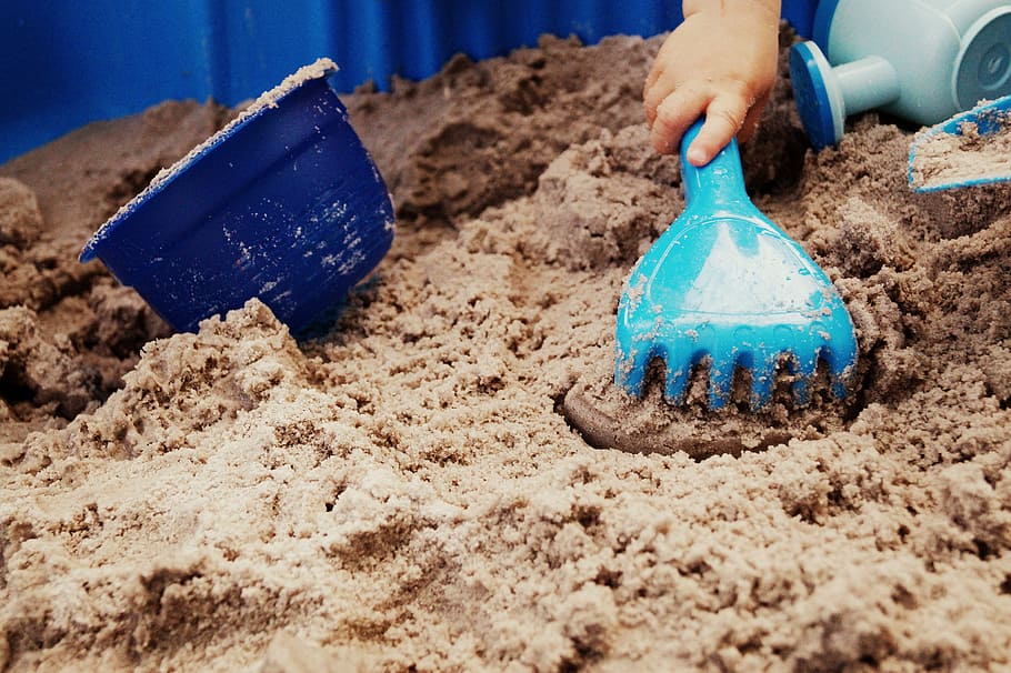 persona, tenencia, azul, rastrillo de arena de plástico, al lado, cangilón, blanco, juguetes, pozo de arena, arena