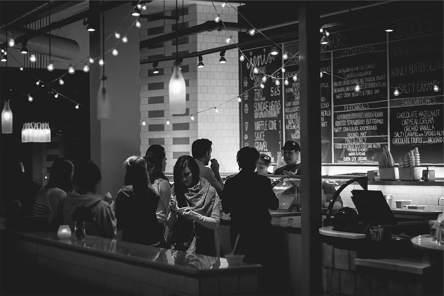 grayscale photo, people, standing, table, near, counter, restaurant, menu, chalkboard, ice cream
