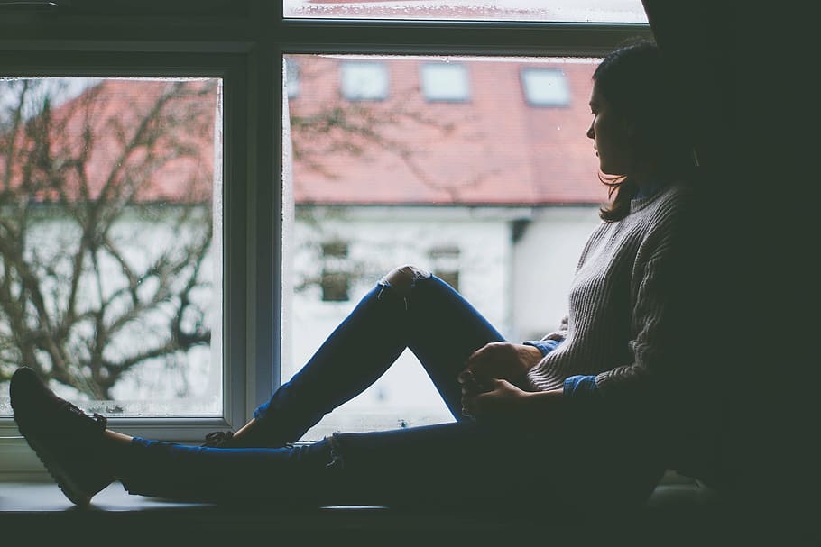 woman, distressed, denim jeans, sweater, leaning, wall post, watching, outside, window, window view