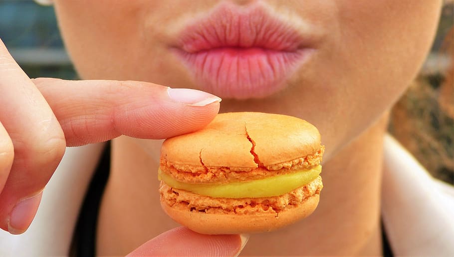 person, holding, macaroon, daytime, macaron, orange, sweetness, pastries, mouth, lips