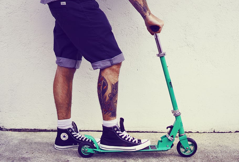 person rides, teal kick scooter, scooter, man, guy, tattoos, tattooed, shorts, trainers, sneaker
